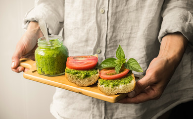 Hands holding a wooden plate with a sandwich with tomato and pesto sauce