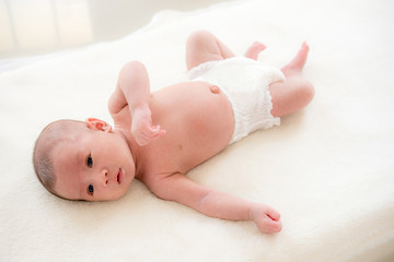 Lovely shirtless newborn Asian baby girl wearing diaper lying on white sheet