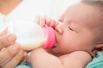 Sleepy cute newborn baby drinking milk from bottle