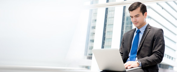 Fototapeta premium Businessman sitting and using laptop computer outdoors in the city
