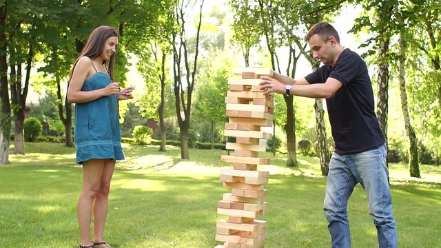 Pair of young people plays jenga large blocks in a Park on an active date. Active logic outdoor games. Guy tries to keep the jenga tower. Slow motion.