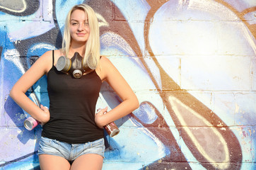 A smiling young and beautiful sexy girl graffiti artist with a paint spray and gas mask on her neck...