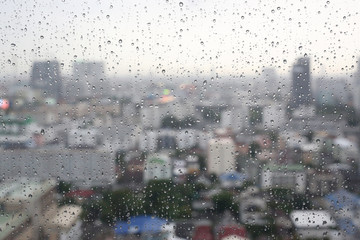 Water rain drops on window glass against blur image of building in bangkok city in thailand at the evening, Rainy day.