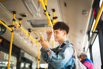 Asian man taking public transport, standing inside bus.