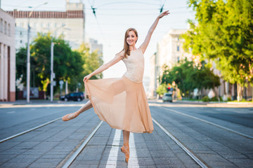 Ballerina in leotard and skirt and ballet shoes dancing on the street, jumps and bends
