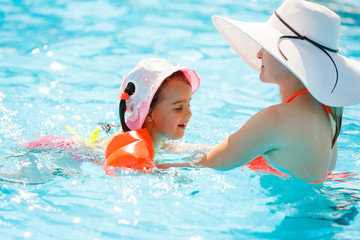 Mother and child swimming in the pool. Happy young woman teaching her daughter to swim. Little kid learning and exercising in the water.