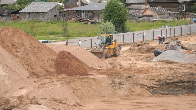 Yellow bulldozer working on a large pile of sand. Superintendents dressed in white helmets solve problems of construction in summer