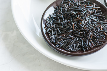 Black rice in a plate on white stone background. Toned.