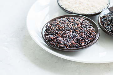 Set of various rice in plates on white stone background: black, basmati and brown rice. Toned.