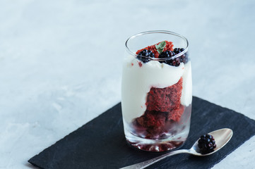 Red velvet sponge cake with cream cheese decorated with fresh berries - dessert in a glass. White stone background.