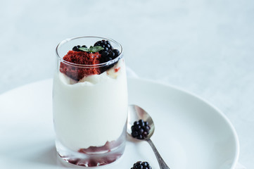 Red velvet sponge cake with cream cheese decorated with fresh berries - dessert in a glass. White stone background.