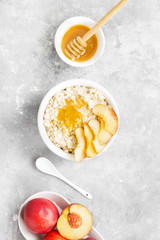 Obraz na płótnie Canvas Oatmeal with nectarine and honey on a gray background. Top view. Food background. Toning