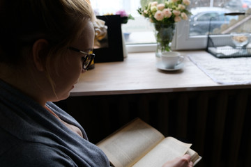 beautiful young woman reading interesting book while drinking tea at home, in cafe