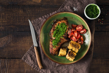 Grilled steak with chimichurri sauce and tomatoes over wooden table