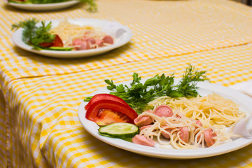 Pasta with sausage and tomatoes with greens on a white plate
