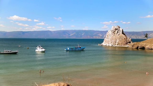 View of the Baikal Bay Shamanka in summer day. Ships and yachts. Tourists swimming in bay in sunny summer day. Olkhon Island, Baikal, Russia, Siberia.