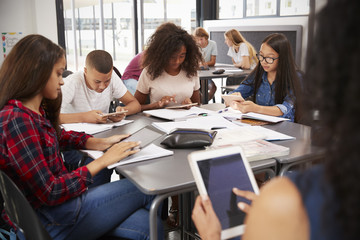 Obraz na płótnie Canvas Teacher sitting with high school students using tablets
