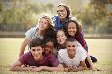 Group of teenage friends lying in a pile on grass