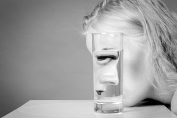 sad girl profile and glass with water on gray background with copy space, monochrome