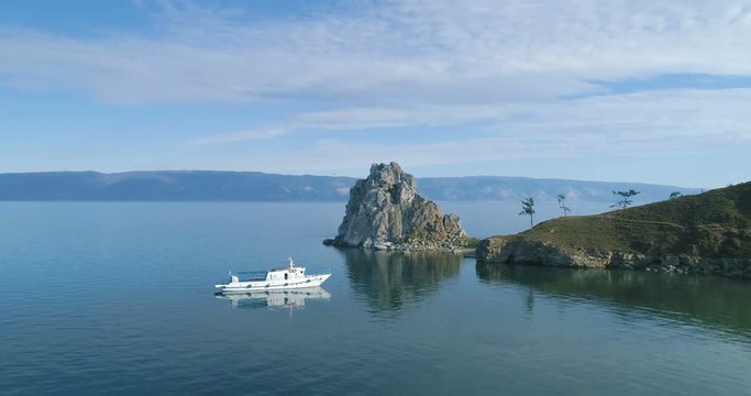 Tranquil Aerial View of the Baikal Bay Shamanka. White ship in calm bay at great lake. Olkhon Island, Baikal, Russia, Siberia. Drone footage. UNESCO World Heritage Site. A famous tourist site. 