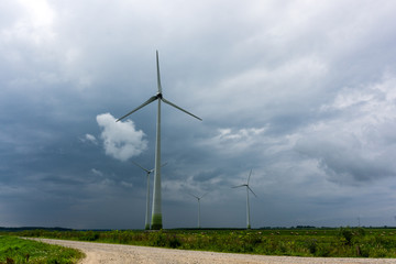 Fototapeta na wymiar Wind Turbines and green fields with hay rolls on a cloudy day. Near storm