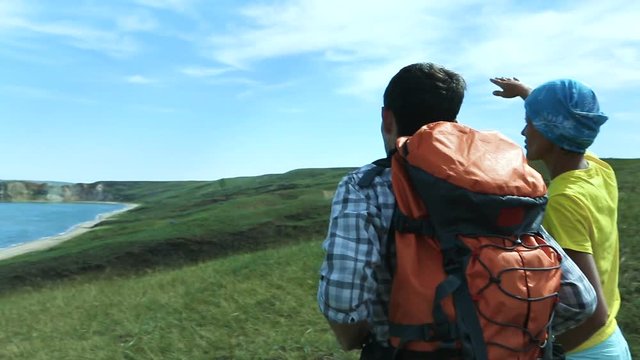Hikers man and woman trekking walking with backpacks along Lake Baikal pointing at blue lake