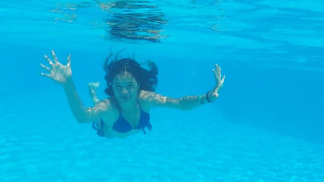 A girl under the water in the pool waving her hands. Beautiful girl in the pool.