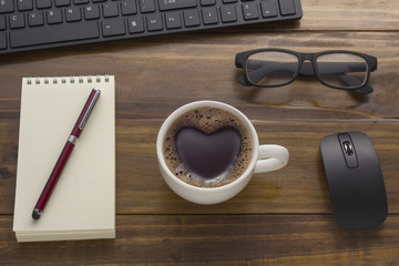 office table with business objects, coffee, notepad, notebook, computer Key broad. Mouse, Glasses. Love sign, Heart shape on Black coffee cup on office table - Top view