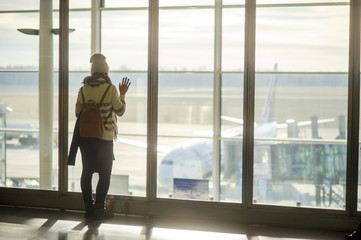 A woman with a backpack standing at the large window in the airport.