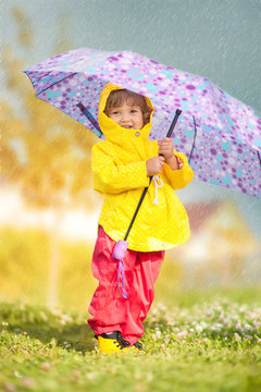 Rainy day. Happy toddler girl wearing waterproof coat with umbrella