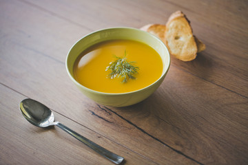 Pumpkin and carrot soup with crackers and parsley on wood background with Spoon and toasted bread slices