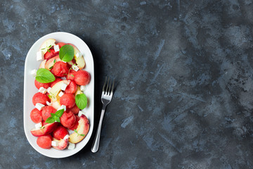 summer watermelon salad with feta, peach and mint on concrete, slate or stone background.