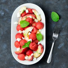 Light summer watermelon salad with feta, peach and mint on concrete, slate or stone background.  Top view space for text. 