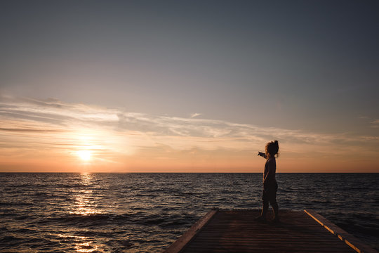 Kleines M&auml;dchen auf Steg am Meer bei Sonnenuntergang