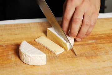 Man slicing brie cheese on the kitchen board