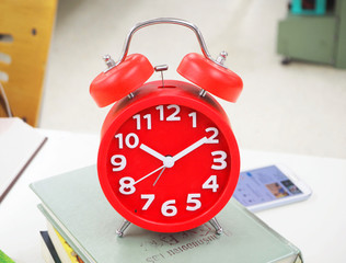 Red clock superimposed on a pile of books stacked in the library.