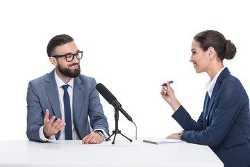 smiling female journalist writing in notepad and interviewing businessman, isolated on white