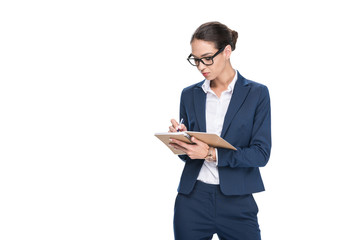 beautiful concentrated businesswoman in suit writing in diary, isolated on white