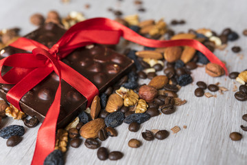  Chocolate bar with red ribbon on a pile of almond, walnuts, raisins, hazelnuts and roasted coffee beans background 