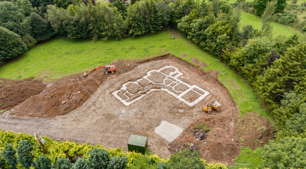 Aerial birds eye view of a new build concrete foundation for a home in the countryside. Green filed with machinery digger and dumper truck.
