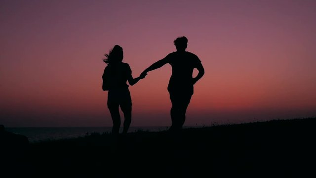 Silhouette of Young Teenage Couple in Love Running and Spinning at Beautiful Pink Sunset. HD Slowmotion Carefree Lifestyle Footage.