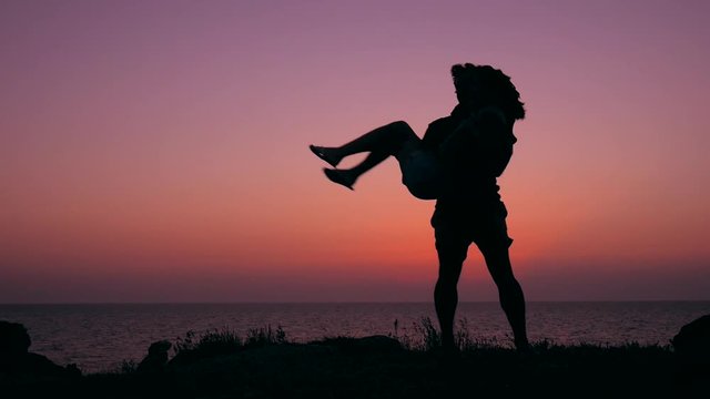 Silhouette of Young Man in Love Holding His Girlfriend and Spinning at Beautiful Pink Sunset Background. HD Slowmotion Carefree Lifestyle Footage.