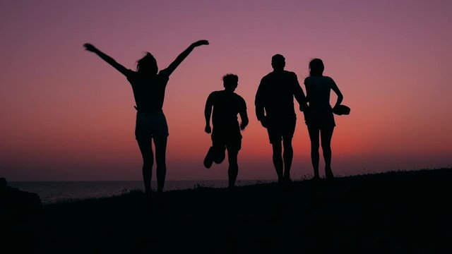Silhouette of Young Mixed Race Teenagers Running and Jumping at Amazing Sunset. HD Slowmotion Carefree Lifestyle Footage.