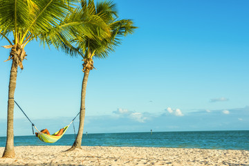 Hammock between two palm trees with a resting man on a deserted beach by the ocean. A beautiful tropical kind of holiday. USA. Florida.Key West
