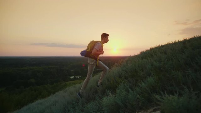 The guy the teenager with a backpack climbs up the mountain. At sunset. Active way of life since youth