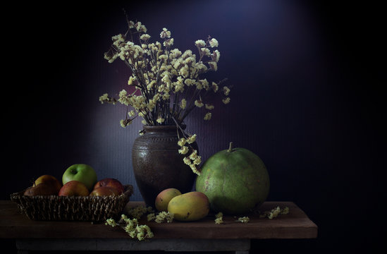 Still Life image of dry flowers in the jar and fruits rotten in basket, All put on the wooden plank in dim light room