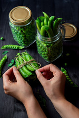 Women's hands tying a rope on bunch of fresh pods of green peas on black wooden background. Bio healthy food background
