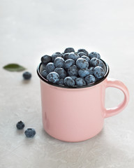 Fresh blueberries in pink cup on light gray stone background.