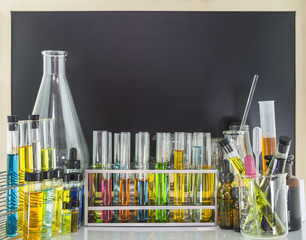 Laboratory glass test tubes in test tubes rack and chemical vials with colorful chemical by the blank blackboard is the scene behind, science background