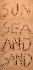 Sun sea and sand written in soft wet sand on a beach